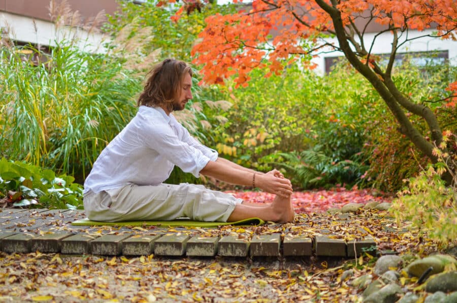 Mann in einer sitzenden Vorwärtsbeuge mit geradem Rücken im herbstlichen Garten – Yoga für die Faszien in der Natur