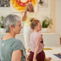 Yogaschülerinnen in einer ruhigen Unterrichtsstunde im Yoga Vidya Ashram, angeleitet von einer Yogalehrerin, während sie ihre passende Yoga Ausbildung finden möchten.
