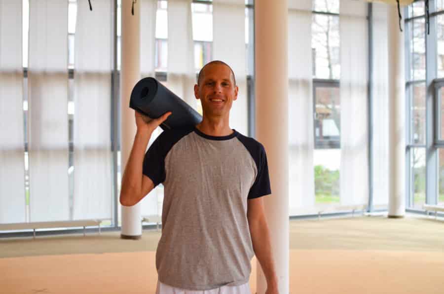 Mann mit Yogamatte geschultert, lächelt in die Kamera