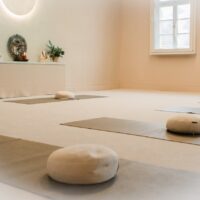 Heller Meditationsraum mit Yogamatten, Meditationskissen, Altar und Fenster mit Tageslicht