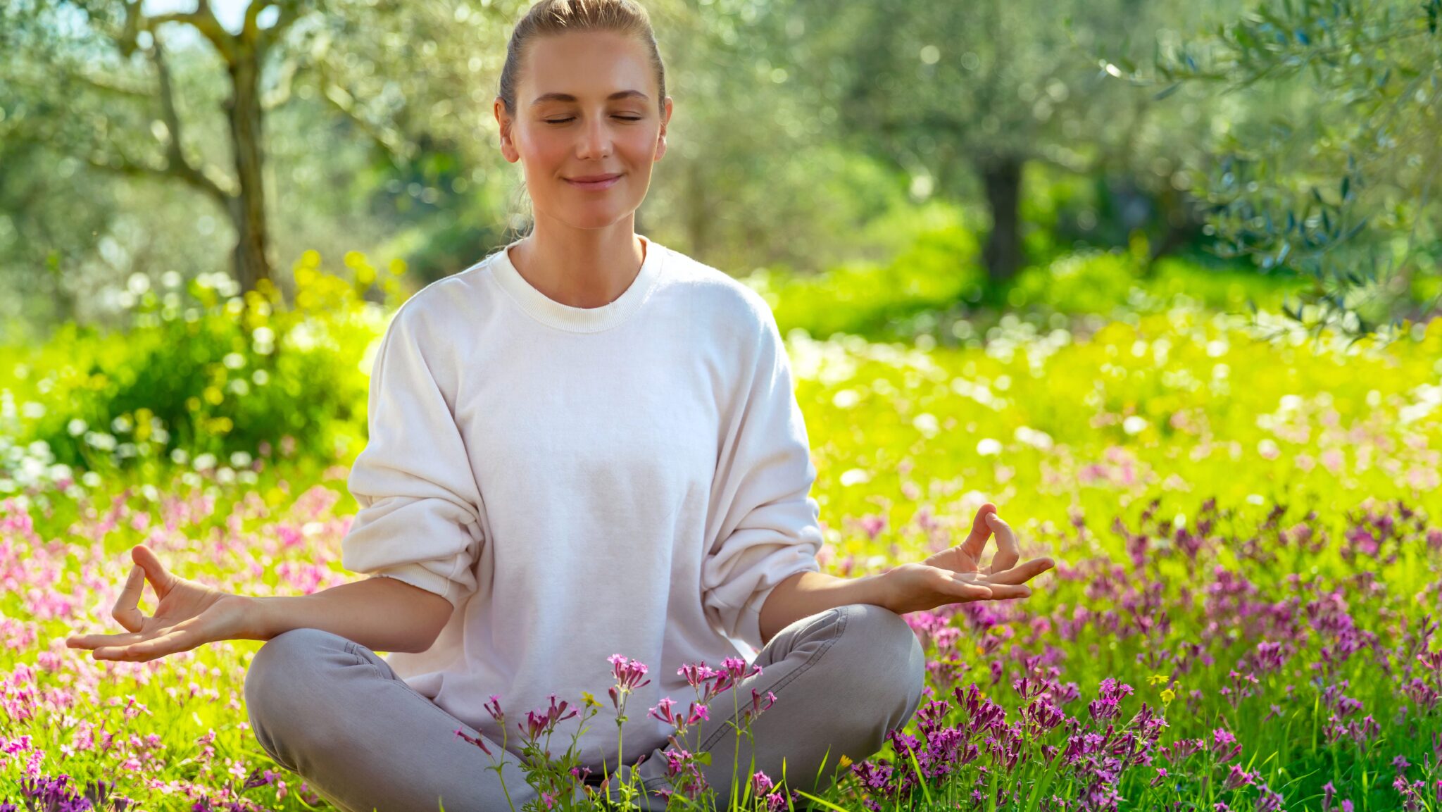 Frau meditiert entspannt auf einer blühenden Wiese im Sonnenlicht, passend zu Yoga-Techniken für den Frühjahrsputz.