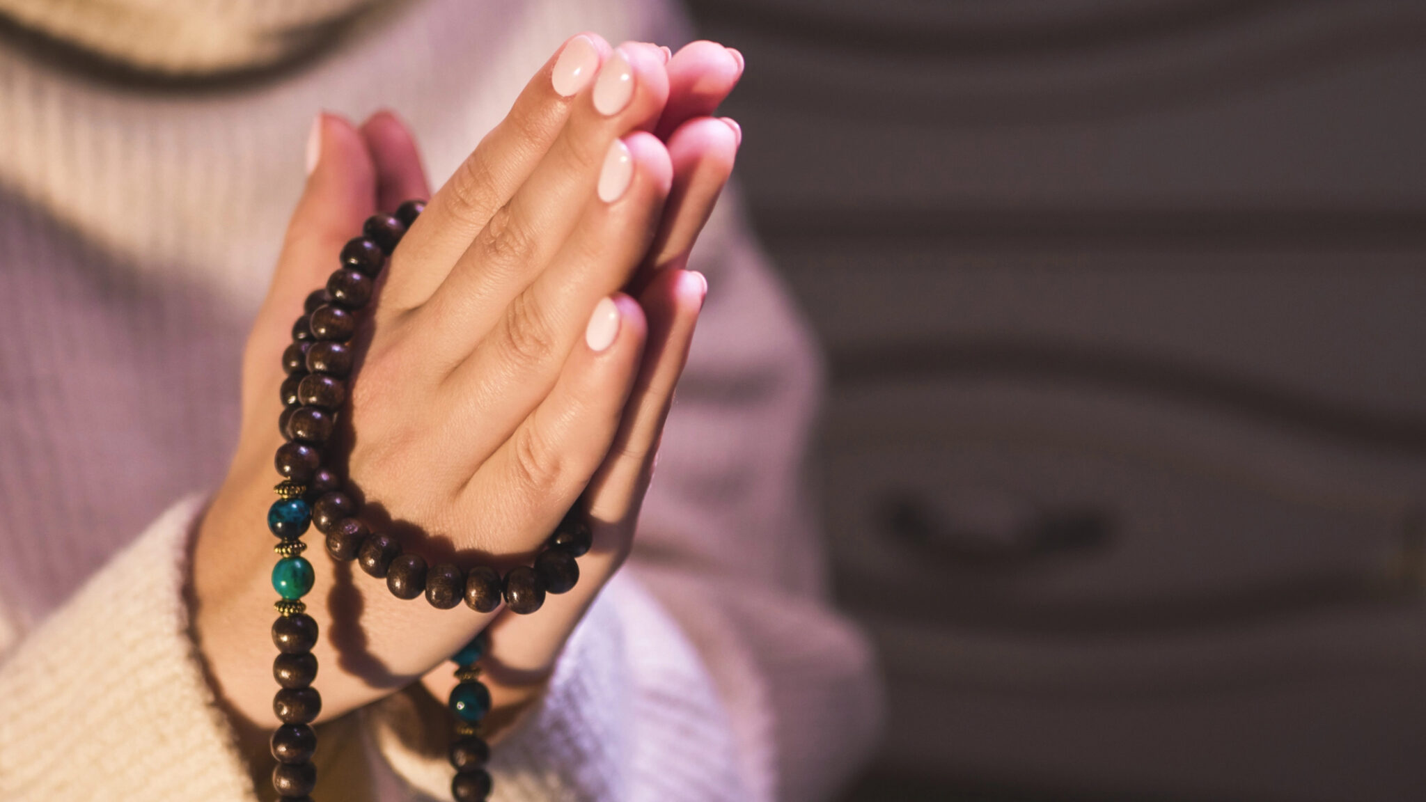 Hände in Gebetshaltung mit einer Mala-Gebetskette als Symbol für Meditation, Gebet und spirituelle Verbindung