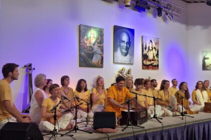 Gruppe von Menschen beim Satsang und Kirtan auf der Bühne im Yoga Vidya Ashram, mit spirituellen Bildern und Jesusbild im Hintergrund