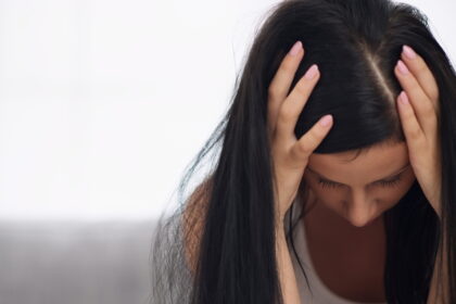 Frau mit gesenktem Blick und Händen am Kopf als Symbol für psychische Belastung, innere Unruhe und depressive Verstimmung