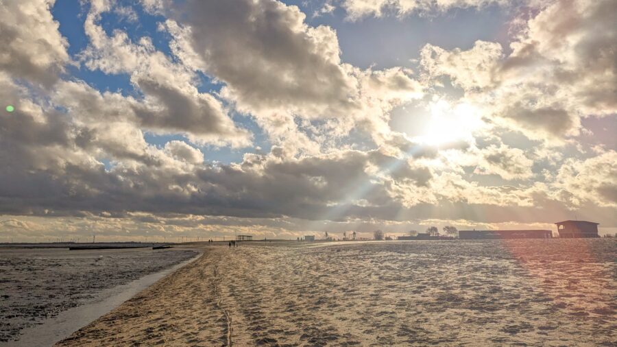 ext:
Sonnenstrahlen brechen durch Wolken über dem Wattenmeer an der Nordsee beim Nordsee-Ashram.