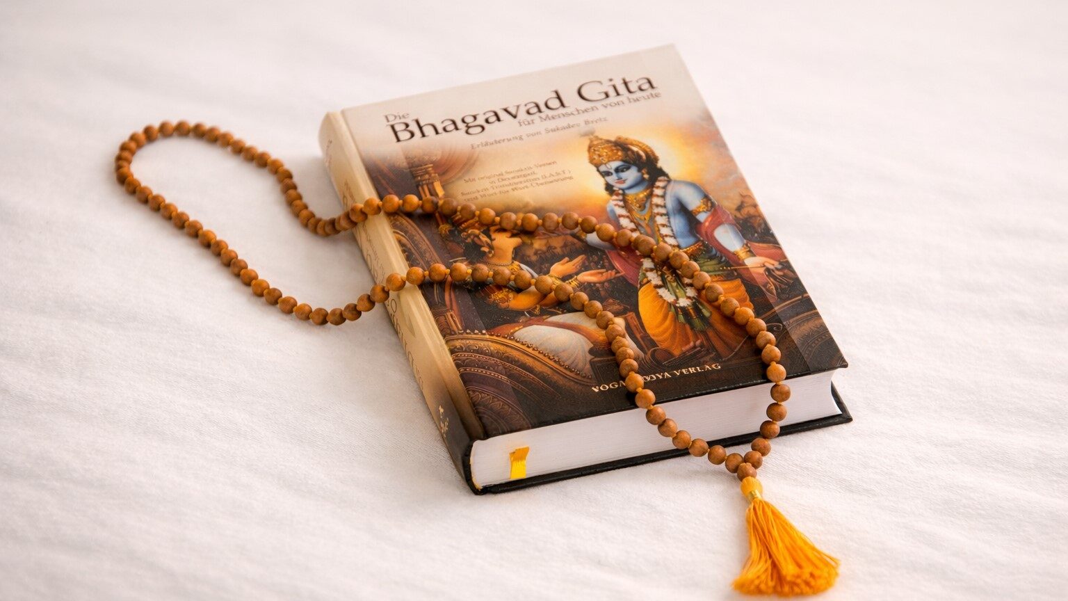 Geschlossene Bhagavad Gita mit Mala aus Holzperlen auf hellem Hintergrund