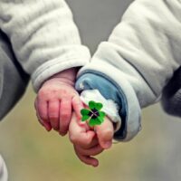 Babys halten Händchen und Kleeblatt