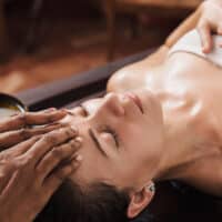 Ayurvedic face massage with oil on the wooden table - Marma Massage